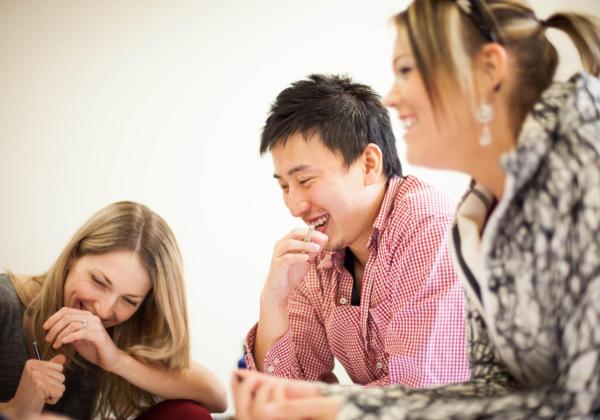 three laughing students sit together at a desk