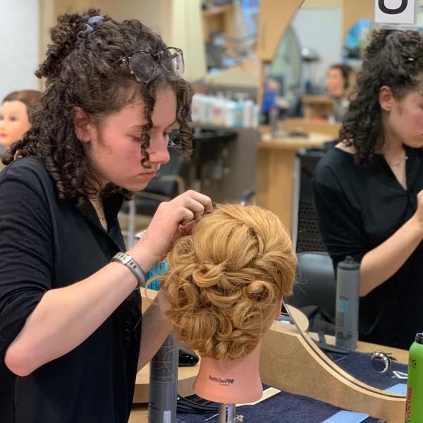 a hairstylist student  pins curls on a mannequin
